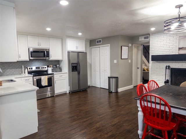 kitchen with appliances with stainless steel finishes, white cabinetry, hanging light fixtures, and dark wood-type flooring