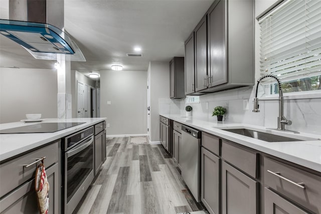 kitchen with tasteful backsplash, stainless steel appliances, extractor fan, sink, and light hardwood / wood-style flooring