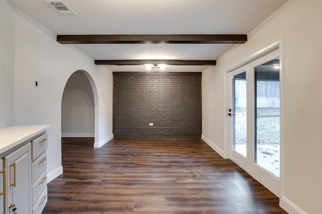 empty room featuring beam ceiling, a healthy amount of sunlight, and dark hardwood / wood-style floors