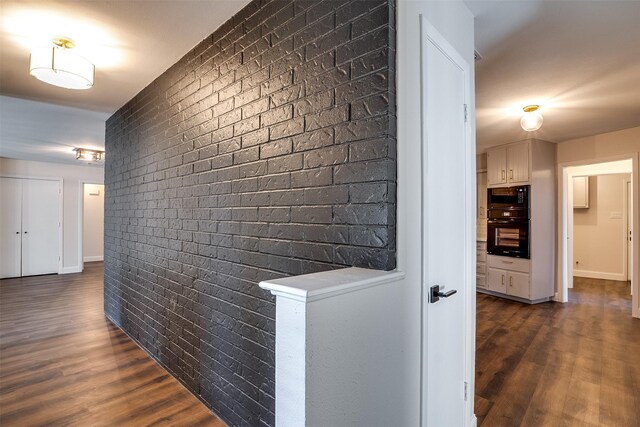 corridor featuring dark hardwood / wood-style flooring and brick wall