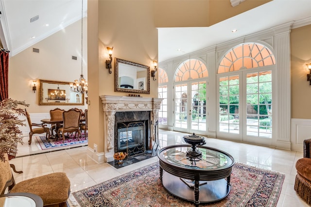 tiled living room featuring french doors, crown molding, an inviting chandelier, a premium fireplace, and a high ceiling