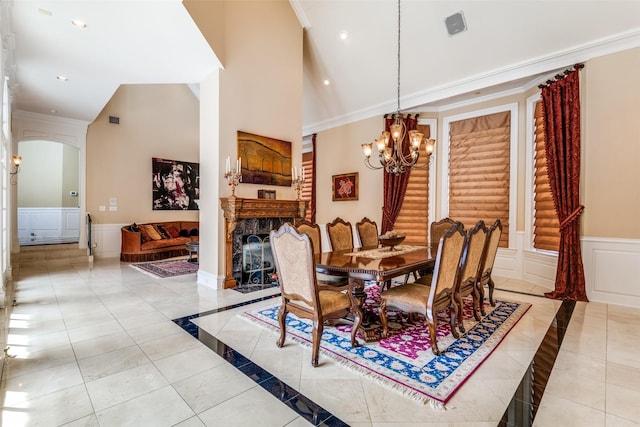 dining space featuring crown molding, a towering ceiling, a notable chandelier, and a high end fireplace