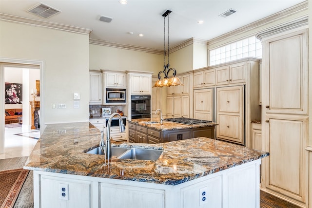 kitchen with appliances with stainless steel finishes, decorative light fixtures, sink, cream cabinets, and a spacious island