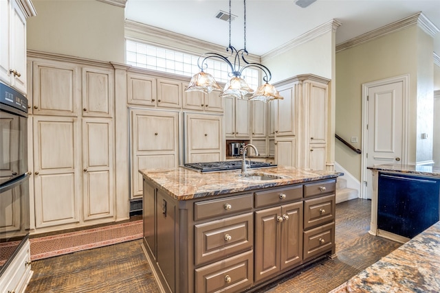 kitchen featuring sink, light stone counters, crown molding, decorative light fixtures, and a kitchen island with sink