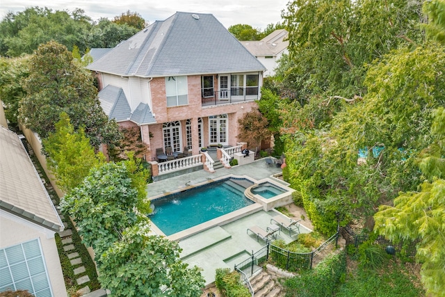 rear view of house featuring french doors, a balcony, a pool with hot tub, and a patio