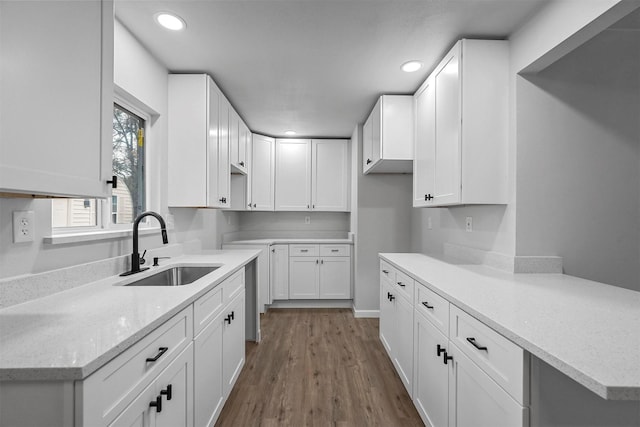 kitchen with light stone countertops, hardwood / wood-style flooring, white cabinetry, and sink