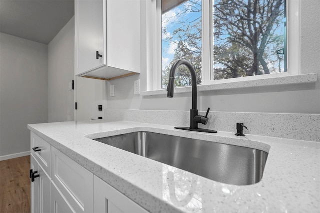 kitchen with white cabinets, light stone countertops, and sink