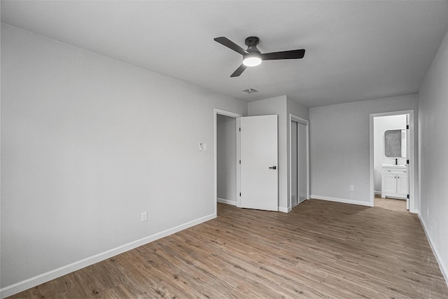 unfurnished bedroom with a closet, ensuite bathroom, light hardwood / wood-style flooring, and ceiling fan