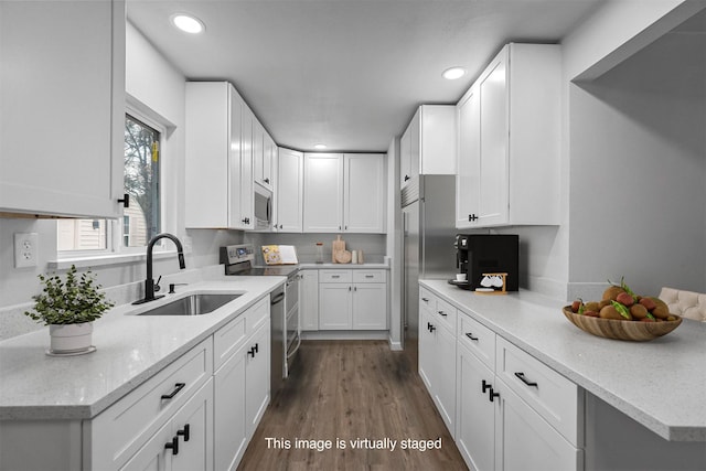 kitchen with light stone countertops, appliances with stainless steel finishes, dark wood-type flooring, sink, and white cabinetry