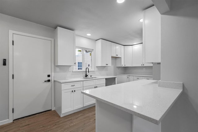 kitchen with light stone countertops, sink, kitchen peninsula, white cabinets, and hardwood / wood-style flooring