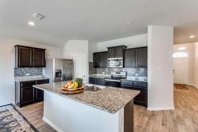 kitchen with backsplash, light hardwood / wood-style flooring, a kitchen island, dark brown cabinetry, and stainless steel appliances