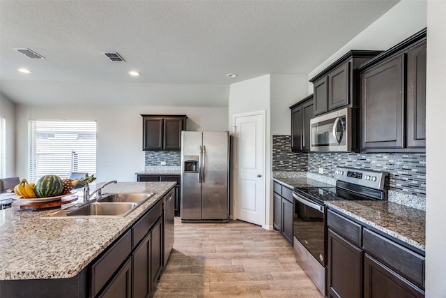 kitchen with sink, decorative backsplash, a center island with sink, appliances with stainless steel finishes, and light wood-type flooring