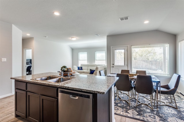 kitchen with light stone countertops, light wood-type flooring, stainless steel dishwasher, sink, and an island with sink