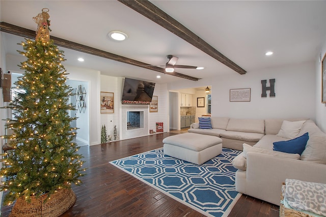 living room featuring beam ceiling, ceiling fan, a large fireplace, and dark wood-type flooring