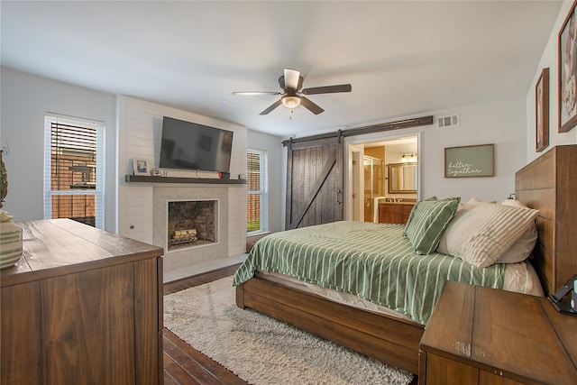 bedroom with ensuite bath, dark hardwood / wood-style floors, ceiling fan, and a barn door