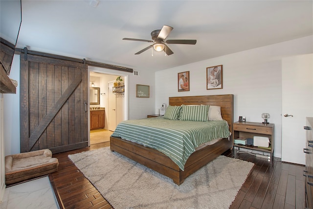 bedroom with dark hardwood / wood-style floors, ceiling fan, connected bathroom, and a barn door