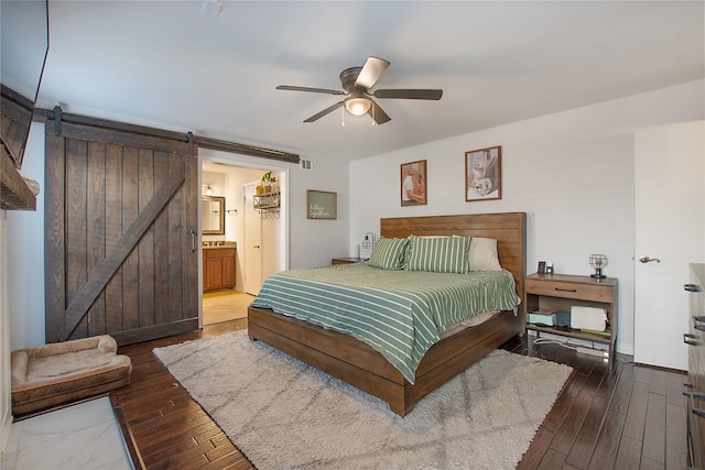 bedroom featuring dark hardwood / wood-style floors, ceiling fan, a barn door, and ensuite bath