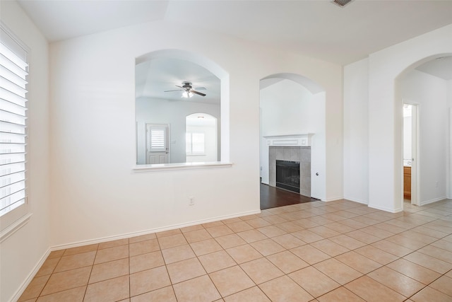 unfurnished living room with light tile patterned floors, a tiled fireplace, a ceiling fan, and baseboards