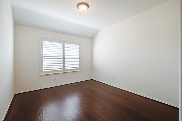 empty room with lofted ceiling, dark wood-style floors, and baseboards