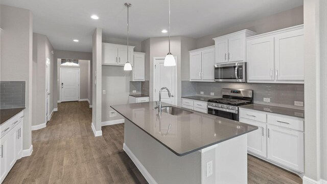 kitchen with sink, hanging light fixtures, stainless steel appliances, an island with sink, and white cabinets