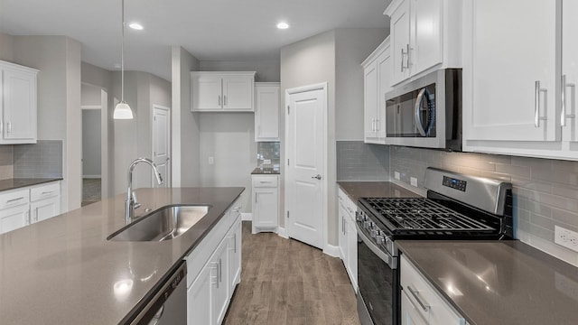 kitchen with sink, hanging light fixtures, stainless steel appliances, wood-type flooring, and white cabinets