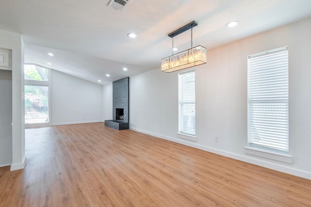 unfurnished living room featuring lofted ceiling, a brick fireplace, a textured ceiling, and light wood-type flooring