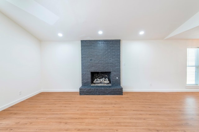 unfurnished living room with lofted ceiling, a fireplace, and light wood-type flooring