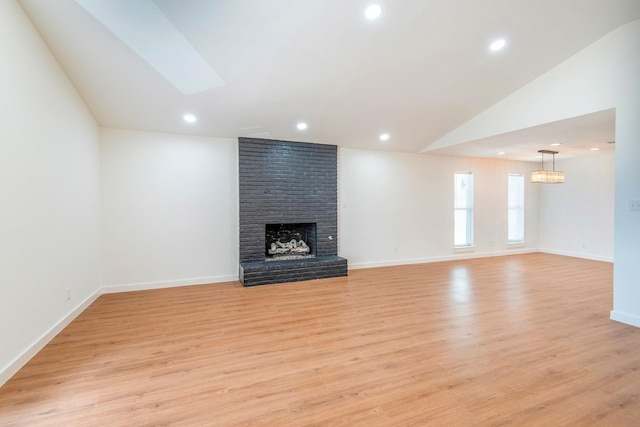 unfurnished living room with lofted ceiling, light hardwood / wood-style floors, and a brick fireplace