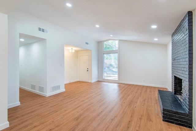 unfurnished living room featuring a brick fireplace, vaulted ceiling, and light wood-type flooring