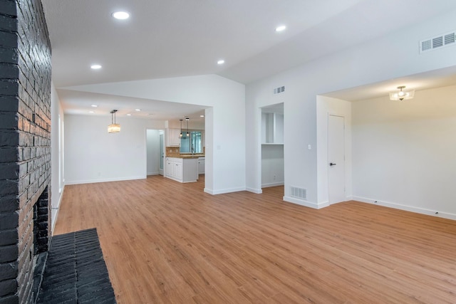 unfurnished living room with lofted ceiling, a brick fireplace, and light wood-type flooring