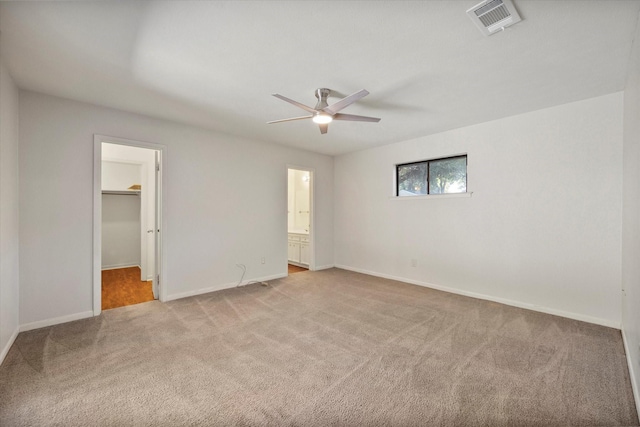 unfurnished bedroom with ceiling fan, a spacious closet, light colored carpet, and ensuite bath