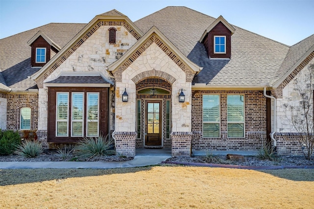 french country home featuring stone siding, brick siding, and a shingled roof