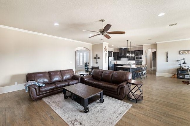 living room with a textured ceiling, ceiling fan, ornamental molding, and dark hardwood / wood-style flooring