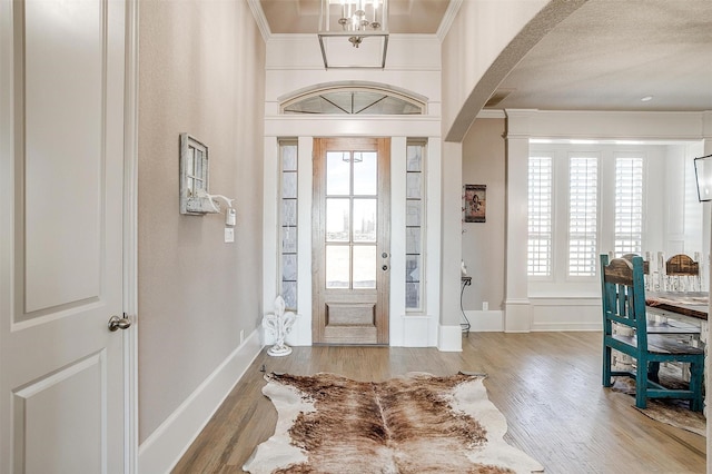 foyer featuring arched walkways, ornamental molding, light wood-style flooring, and baseboards