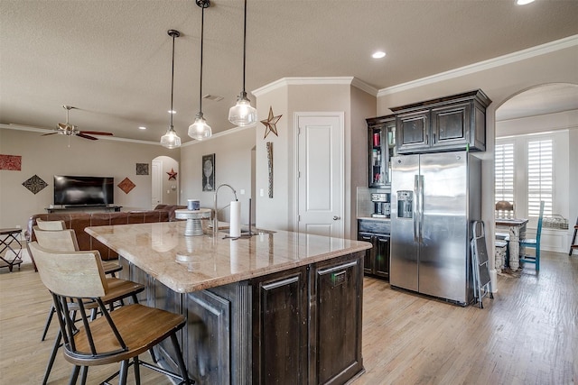 kitchen with stainless steel fridge, a center island with sink, arched walkways, a kitchen bar, and pendant lighting