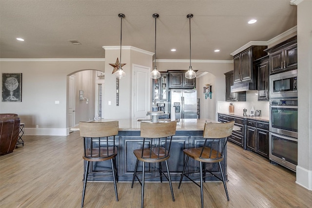 kitchen featuring arched walkways, a kitchen island, appliances with stainless steel finishes, hanging light fixtures, and dark brown cabinets