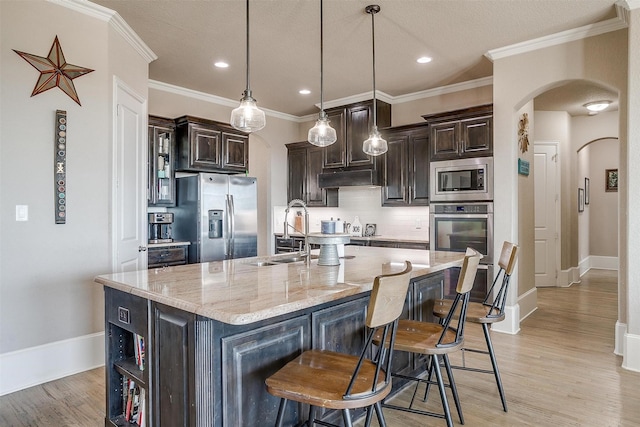 kitchen with arched walkways, an island with sink, appliances with stainless steel finishes, pendant lighting, and a sink