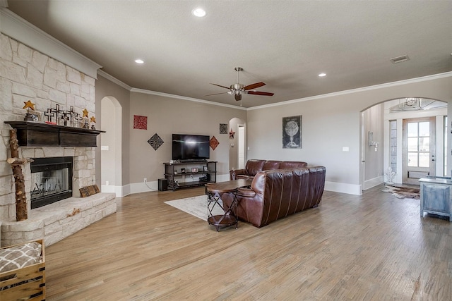 living room featuring arched walkways, light wood-type flooring, a fireplace, and visible vents