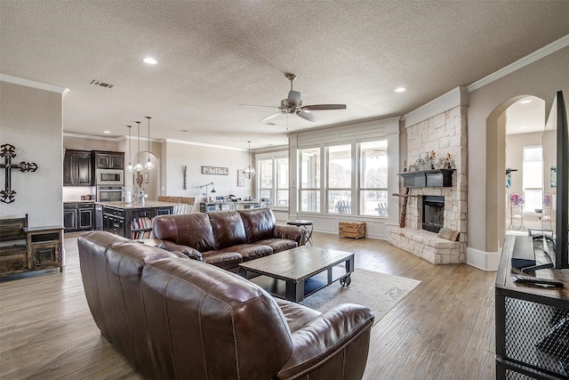 living area with a textured ceiling, a stone fireplace, visible vents, light wood-style floors, and ornamental molding