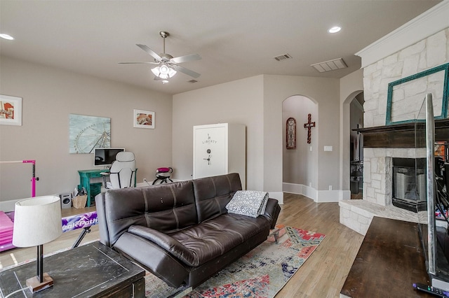 living area featuring arched walkways, visible vents, light wood-style flooring, ceiling fan, and a fireplace