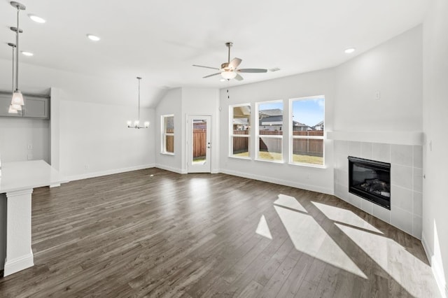 unfurnished living room featuring ceiling fan with notable chandelier, dark wood-type flooring, a tiled fireplace, and vaulted ceiling