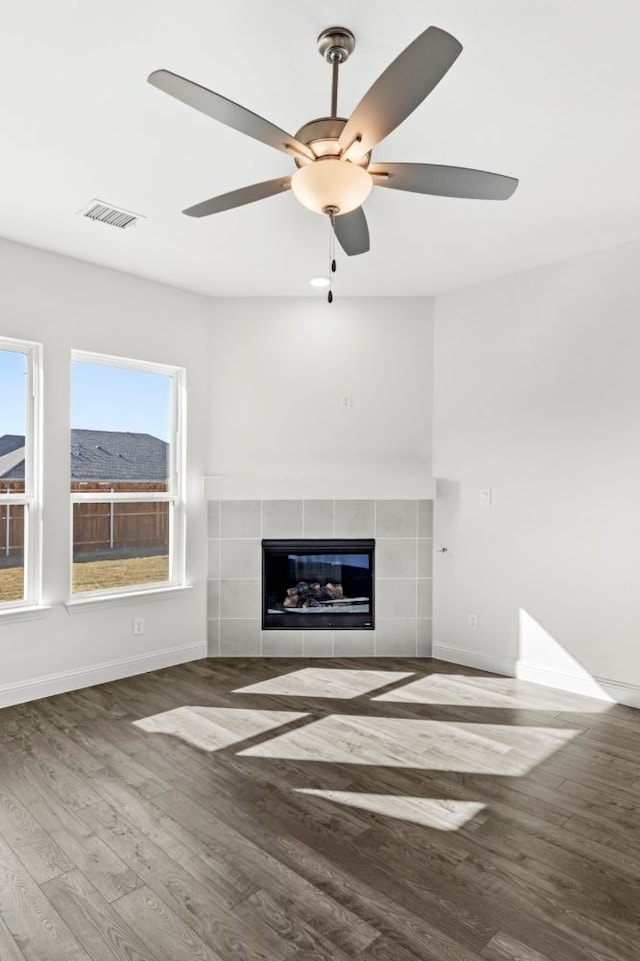 unfurnished living room featuring ceiling fan, wood-type flooring, and a tiled fireplace