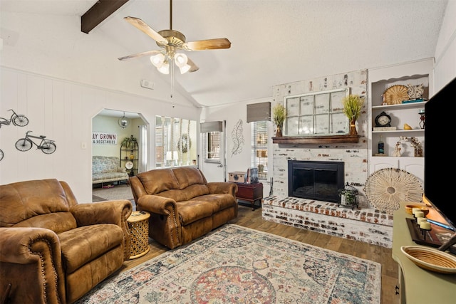 living room with ceiling fan, hardwood / wood-style floors, lofted ceiling with beams, and a brick fireplace