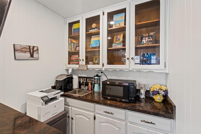 bar with white cabinets, wood walls, sink, and a textured ceiling