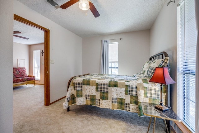 bedroom with ceiling fan, light colored carpet, and a textured ceiling