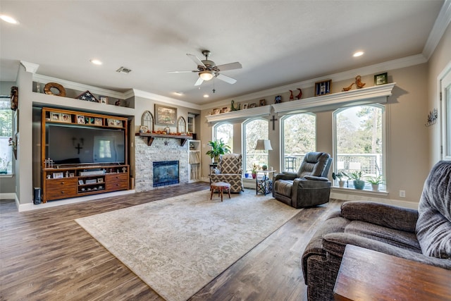 living room featuring a stone fireplace, crown molding, hardwood / wood-style floors, and ceiling fan