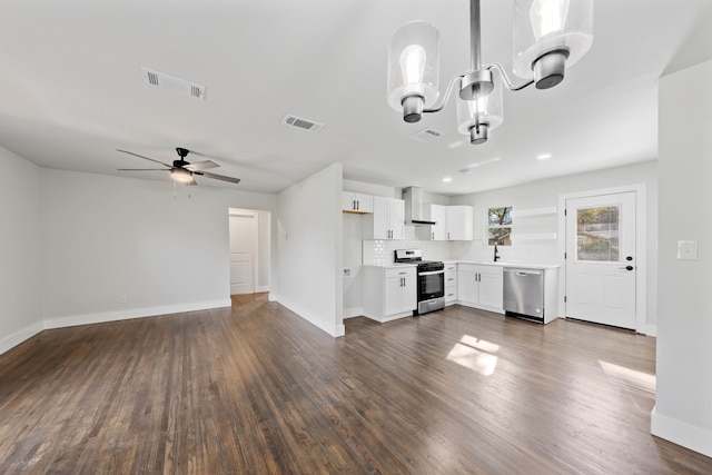 kitchen with white cabinets, ceiling fan, wall chimney exhaust hood, appliances with stainless steel finishes, and dark hardwood / wood-style flooring