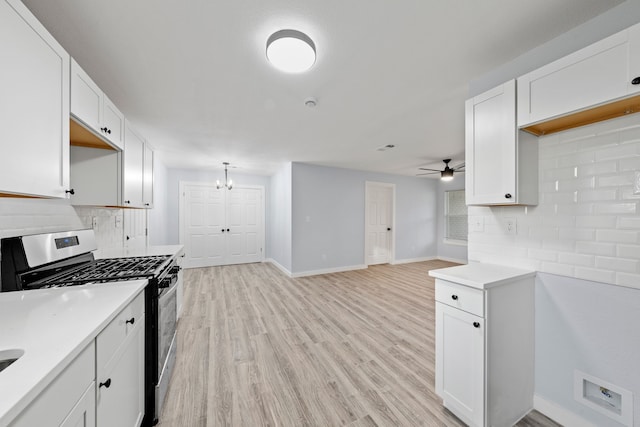 kitchen featuring light wood-type flooring, tasteful backsplash, stainless steel gas range, ceiling fan with notable chandelier, and white cabinetry