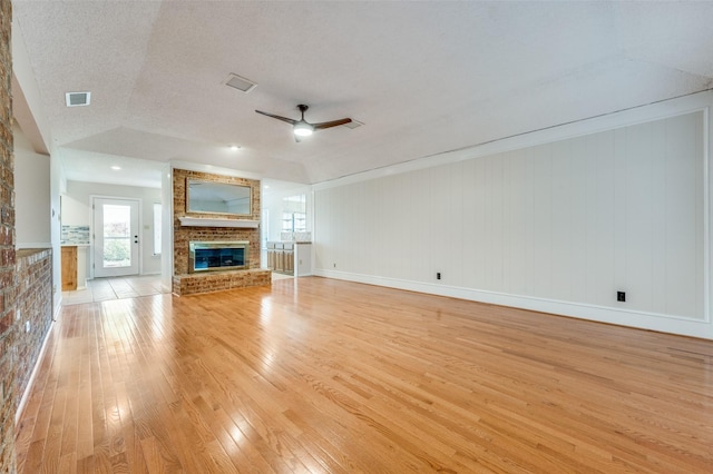 unfurnished living room with a textured ceiling, vaulted ceiling, ceiling fan, light hardwood / wood-style flooring, and a fireplace