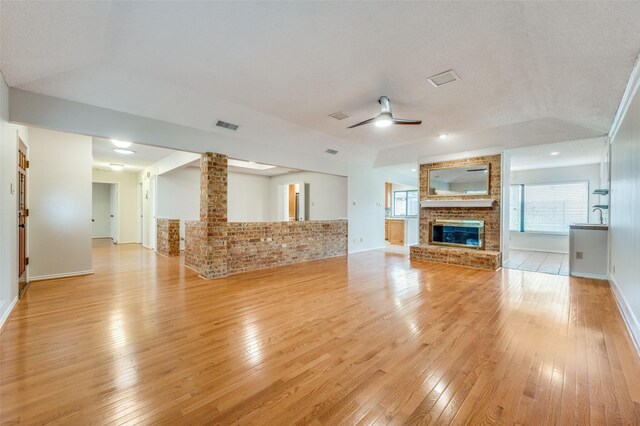 unfurnished living room with light wood-type flooring, a brick fireplace, a textured ceiling, vaulted ceiling, and ceiling fan